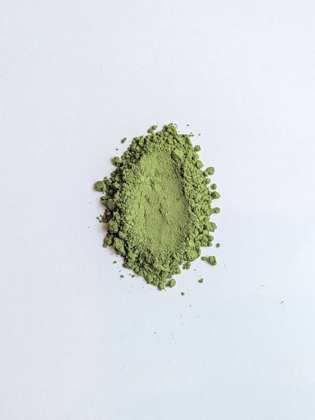 A mound of fresh, vivid green matcha powder on a white background