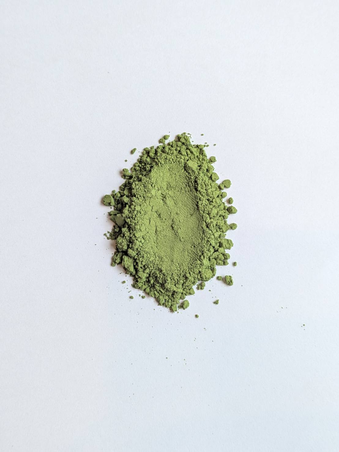 A mound of fresh, vivid green matcha powder on a white background